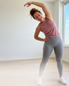Sportieve vrouw rekt zich uit in grijze push-up legging met telefoonzak