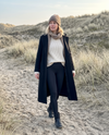 Vrouw in de zwarte Contoura Thermo Shaping Legging met wollen jas en muts tijdens een winterwandeling in de duinen