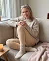 Vrouw in de nude Contoura Thermo Shaping Legging met gebreide trui en thee op de bank
