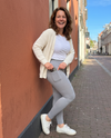 Lachende vrouw in grijze push-up legging met telefoon in de zak voor een terracotta muur