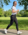 Sportieve vrouw jogt lachend in zwarte push-up legging met telefoonzak